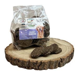 Pack of Rabbit burger dog treats displayed on a log with some loose in front