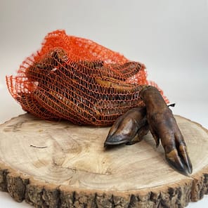 A bulk pack of Wild Boar Trotters natural dog chews in orange netting on a rustic log - MAH Pet Supplies