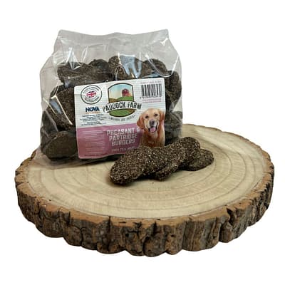 Pack of Pheasant and Partridge Burger Dog treats displayed on a log with 4 loose burgers out of packet