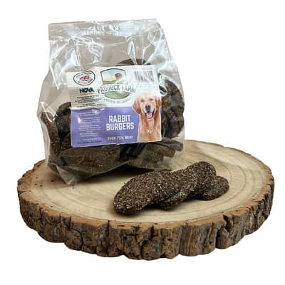 Pack of Rabbit burger dog treats displayed on a log with some loose in front